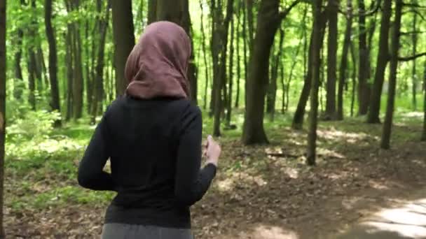 Jeune fille athlétique en hijab courir, faire du jogging dans le parc vert, forêt, vue de dos 50 images par seconde — Video