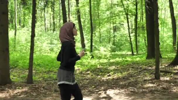 Jeune fille athlétique en hijab courir, faire du jogging dans un parc vert, vue latérale 50 fps — Video