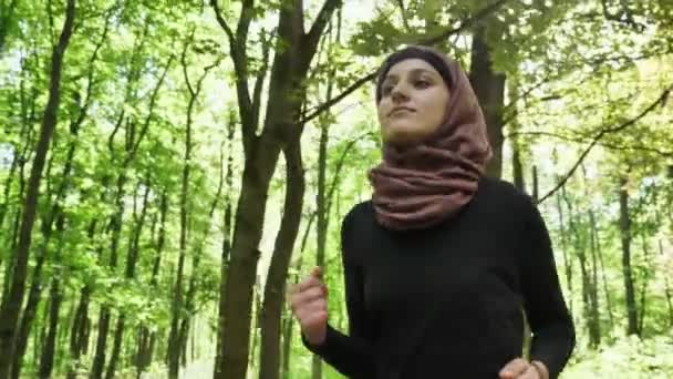 Jovem atlética em hijab running, correndo no parque verde, floresta, vista frontal 50 fps — Vídeo de Stock