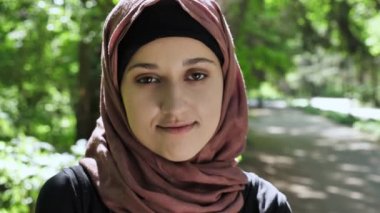 Gülümseyerek, kamera, park içinde belgili tanımlık geçmiş bakarak sevimli bir genç kız bir hijab ın portresi. 50 fps