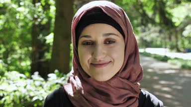 Gülümseyerek, kamera, park içinde belgili tanımlık geçmiş bakarak sevimli bir genç kız bir hijab ın portresi. 50 fps