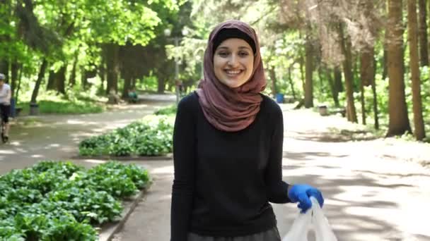 Plogging concept, young girl in hijab runs through park and cleans up garbage, shiwing like sign. 50 fps — Stock Video