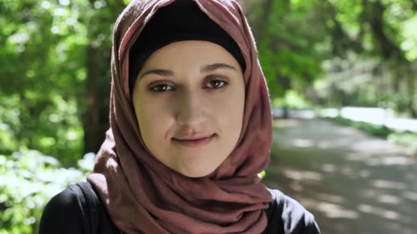 Portrait of a cute young girl in a hijab, smiling, looking at the camera, park in the background. 50 fps — Stock Video