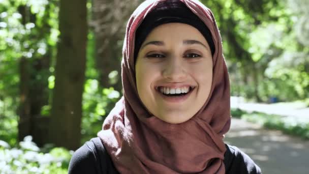 Portrait of a cute young girl in a hijab, smiling, looking at the camera, park in the background. 50 fps — Stock Video