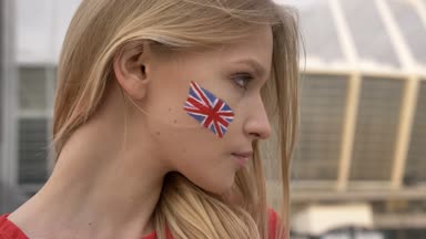 Genç sarışın kız futbol hayranı bakarak kamera, gülümseyen, ciddi bir yüz, stadyum içinde belgili tanımlık geçmiş içine İngiltere'nin portresi 50 fps