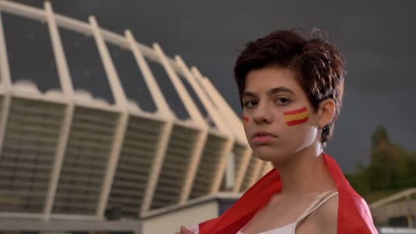 Retrato de una joven aficionada al fútbol morena en España, mirando a la cámara, cara seria, estadio nocturno al fondo 50 fps — Vídeo de stock