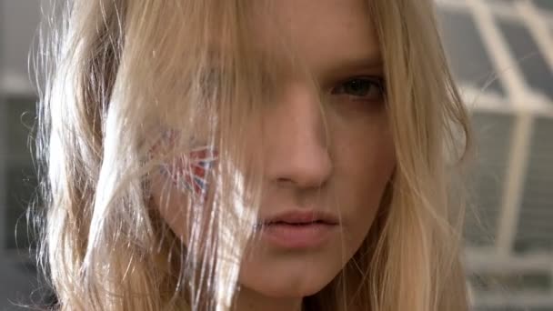 Portrait of a young blonde girl soccer fan of England looking into the camera, serious face, stadium in the background 50 fps — Stock Video