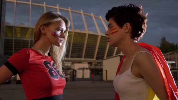 Dos chicas jóvenes, aficionados al fútbol, Inglaterra contra España, confrontación, viento, estadio nocturno en el fondo 50 fps — Vídeo de stock