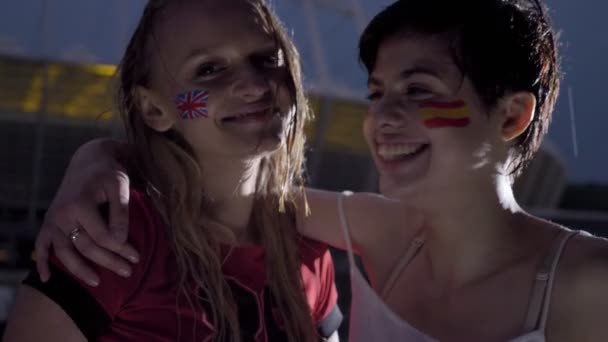 Twee jonge meisjes, voetbalfans in regen, Engeland en Spanje, glimlachen, lachen, omarmen, stadion in de achtergrond 50 fps — Stockvideo