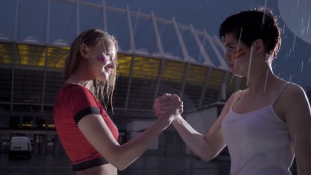 Bajnokok Ligája, két fiatal lányok szurkolók az esőben a kézfogások, konfrontáció koncepció 60 fps — Stock videók