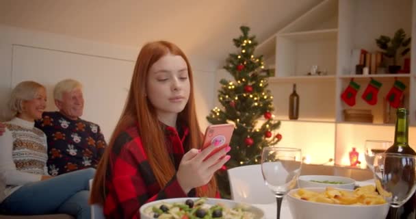Dziadkowie siedzą słodko na kanapie. Wnuczka używa smartfona na Boże Narodzenie — Wideo stockowe