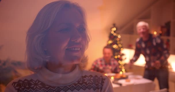 Grandmother looks out the window Christmas family dinner evening behind glass cozy — ストック動画