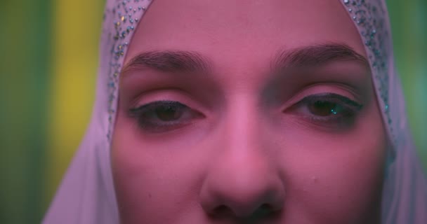 Close-up of eyes in white hijab Caucasian young girl green background neon light — Stok Video