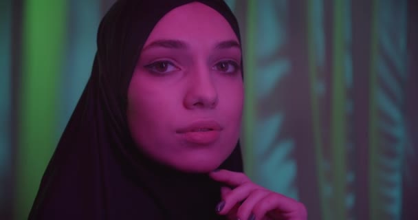 Paars licht portret zwart hijab pensive blik op de camera close-up Kaukasische meisje schittert — Stockvideo