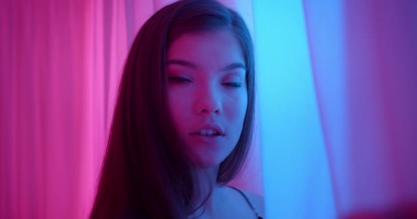 Mädchen in Neon blickt in die Kamera um die Ecke Licht Nachtporträt flirtet Vorhänge rosa blau — Stockvideo