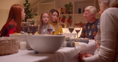Büyük aile yemeği konuşuyor anne Noel ağacı konuşuyor farklı nesiller büyükanne torun büyükbaba ve kırmızı kız kardeş gülüyor