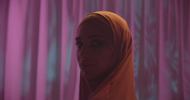 Καυκάσια νεαρή κοπέλα σε hijab νέον πορτοκαλί χρώμα ροζ φόντο πορτρέτο μακιγιάζ κοιτάζοντας κάμερα σκιά νύχτα — Αρχείο Βίντεο