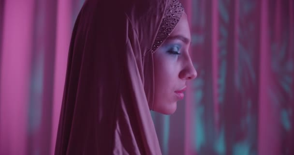 Chica joven caucásica en hijab neón púrpura color fondo retrato maquillaje ver perfil sombra noche — Vídeo de stock