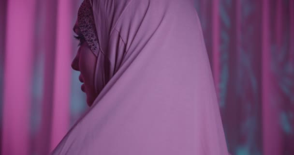 Кавказская девушка в хиджабе неоновый фиолетовый цвет фона портрет макияж вращается в камеру тени ночной макияж — стоковое видео