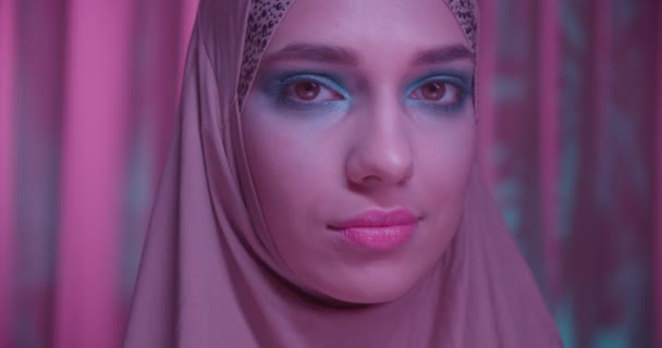 Caucasian young girl in hijab neon purple color background portrait makeup look camera shadow night portrait eyes — Stock Video