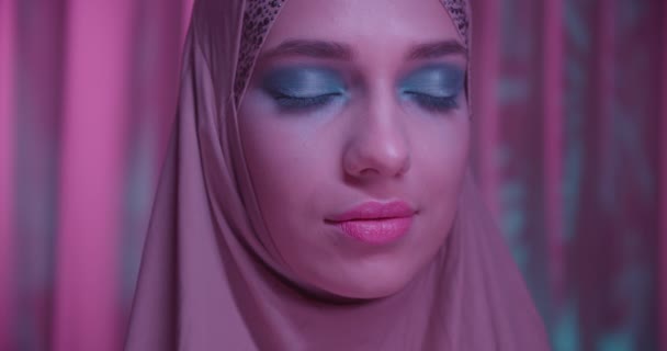 Caucasian young girl in hijab neon purple color background portrait makeup look camera shadow night closed eyes — Stock Video