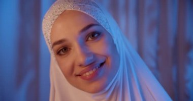 Beyaz tesettürlü beyaz kızın portresi neon ışıklı kameraya bak gece makyajı gülümsüyor.