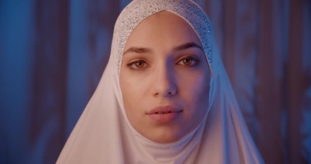 Portrait of caucasian girl in white hijab neon light look at camera serious night make-up — Stok Video