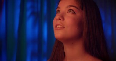 Kafkas 'lı genç bir kızın portresi neon rengi koyu mavi arka plan. Kırmızı ışık yukarı bakıyor.