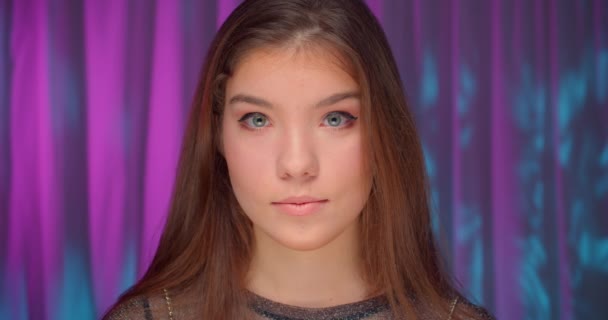 Крупним планом портрет кавказької дівчини в неоновому світлому платті фіолетовий фон впевнений серйозний вигляд посмішка сміх радості — стокове відео