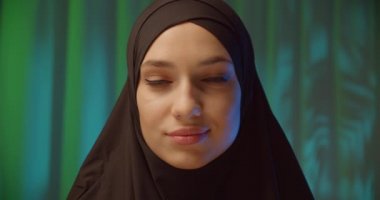 Beautiful confident girl in black hijab neon night green background shadow image make-up smile