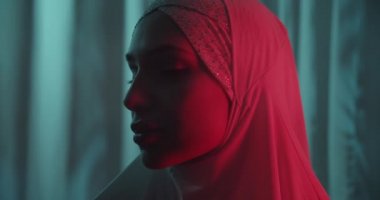 Close-up Beautiful portrait of a confident girl in a white hijab neon tropical background shine view profile make-up portrait red light profile red beam