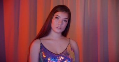 Beyaz, güzel, kendine güvenen bir kız portresi. Neon ışığı. Kamera turuncu arka plan.
