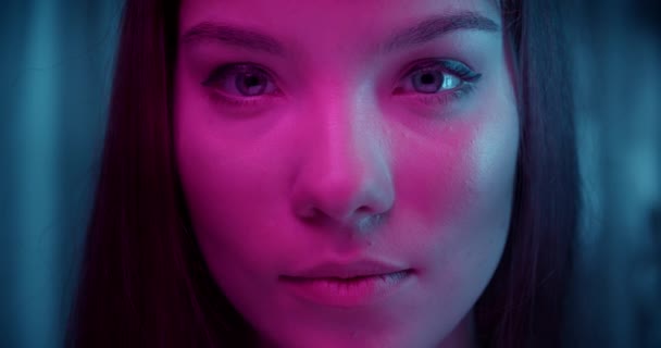 Close-up eyes Portrait of caucasian beautiful confident girl neon light look into camera background evening strong look violet ray — Stock Video