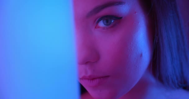 Close-up meisje in neon kijkt naar de camera om de hoek licht nacht portret flirten make-up ogen — Stockvideo