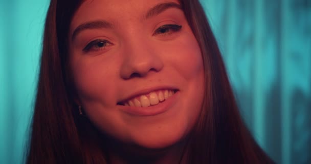 Közelkép szemek kaukázusi fiatal lány portré mosoly narancs arcszín néz kamera flört kék háttér — Stock videók