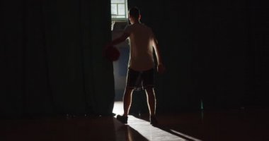 Genç beyaz basketbolcu topu parmağında döndürmeye hazırlanıyor. Parlak ışık. Gölge. Kandırmaca. Profesyonel top sürme. Eğitim.