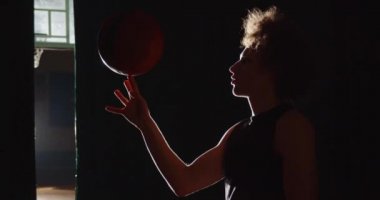 Genç kıvırcık saçlı beyaz basketbolcu hazır oluyor. Silüet topu parmağında döndürüyor. Parlak gölge numarası yapıyor.