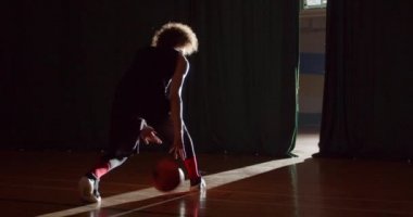 Kıvırcık saçlı beyaz basketbolcu, sahne arkasındaki karanlık siluete girmeye hazırlanıyor.