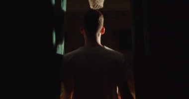 Beyaz tenli genç basketbolcu parket salonundaki stadyuma gidiyor. Sahne arkasındaki spot ışığı ışık huzmesi ışık topu özgüvenini yansıtıyor.