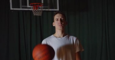 Popüler bir beyaz basketbolcu portresi, kendine güvenen bir görünümün arka planında basket topuyla oynar.