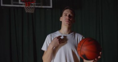 Popüler bir beyaz basketbolcu portresi, kendine güvenen bir arka planda basket topuyla oynar.