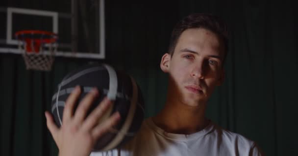 Primer plano Popular jugador de baloncesto caucásico retrato jugando con una pelota de la canasta en un fondo serio confiado look camiseta blanca — Vídeos de Stock