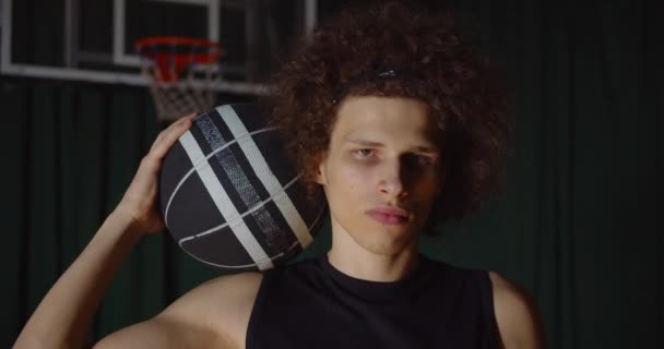 Popular pelo rizado caucásico jugador de baloncesto retrato mirada seria a los fotógrafos de la cámara flash sostiene la pelota — Vídeo de stock