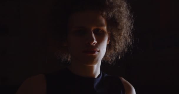 Close-up Popular de cabelos encaracolados jogador de basquete caucasiano retrato olhar sério para fotógrafos câmera flash detém bola escuridão profissional — Vídeo de Stock
