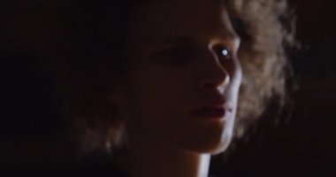 Yakın plan Kıvırcık saçlı beyaz basketbolcu portresi. Kameramanlara ciddi ciddi bak. Flaş topu profesyonel karanlık tutuyor.