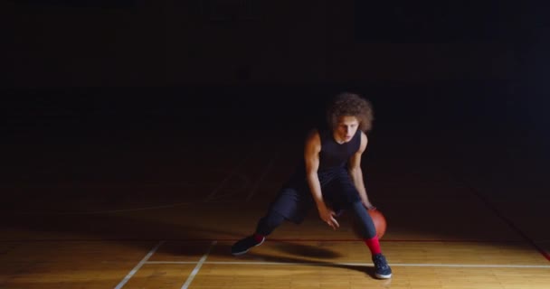 Riccio caucasico giocatore di pallacanestro Dribbling palla macchina fotografica professionale oscurità raggio di luce — Video Stock