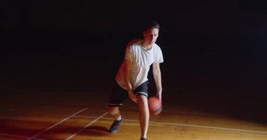 Kafkasyalı basketbolcu, profesyonel bir karanlık kamera ışığıyla top sürüyor.
