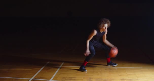 Lockige kaukasische Basketballspieler Dribbling Ball Kamera Professionelle Dunkelheit Strahl des Lichts — Stockvideo