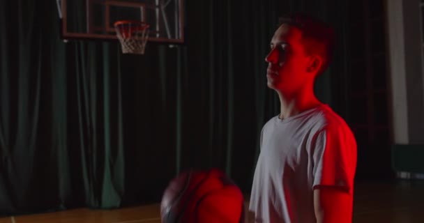 Giovane ritratto di un giocatore di basket caucasico che tiene una palla da basket a luci rosse su uno sfondo fiducioso che si riscalda preparandosi — Video Stock