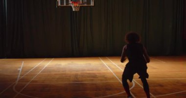 Genç kıvırcık basketbolcu parke oynuyor. Topu potaya atıyor. Gece karanlığında idman yapıyor.